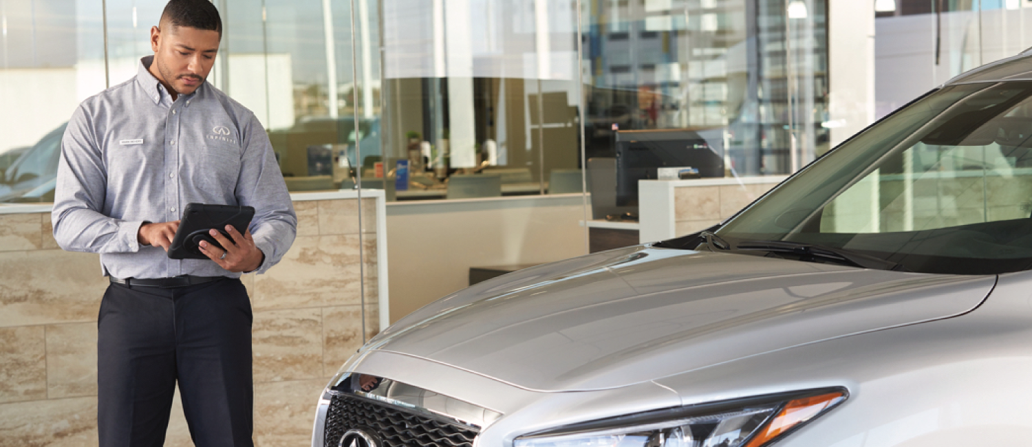 INFINITI Sales associate reviewing vehicle in dealership showroom.